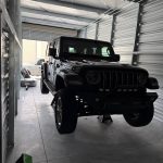 Black Jeep Wrangler lifted on jack stands inside a storage unit during suspension and steering repair work.