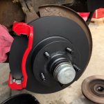 Close-up of a vehicle brake assembly with a new black brake rotor and bright red caliper bracket installed on the wheel hub.