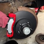 Close-up of a vehicle brake assembly showing a new black brake rotor, bright red caliper bracket, and a brake pad installed on the wheel hub.
