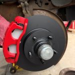 Close-up of a completed vehicle brake assembly with a new black brake rotor, bright red brake caliper, and brake pads installed on the wheel hub.